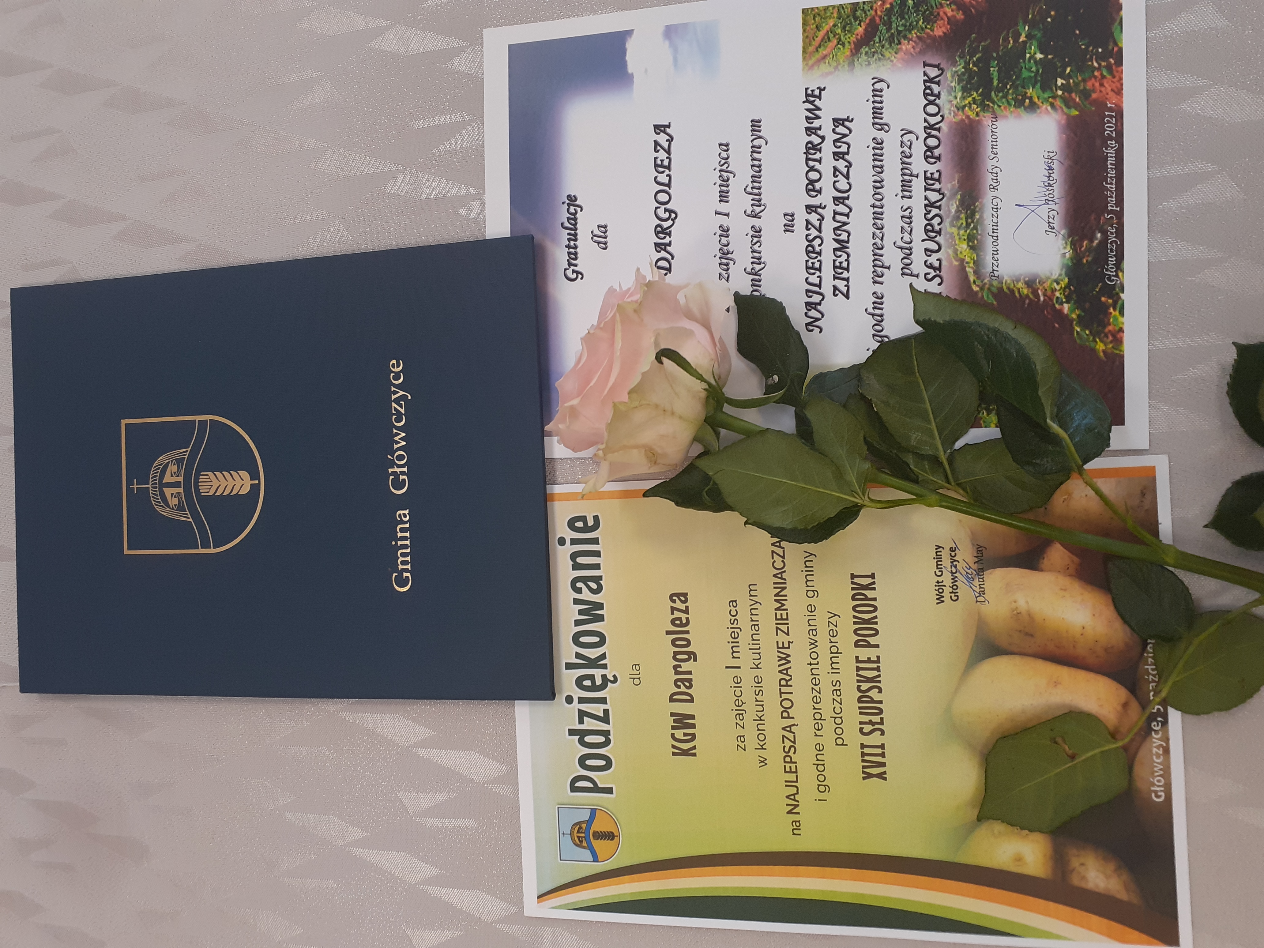 Ułłożone na stole: podziękowanie i gratulacje dla KGW w formie dyplomu oraz róża.