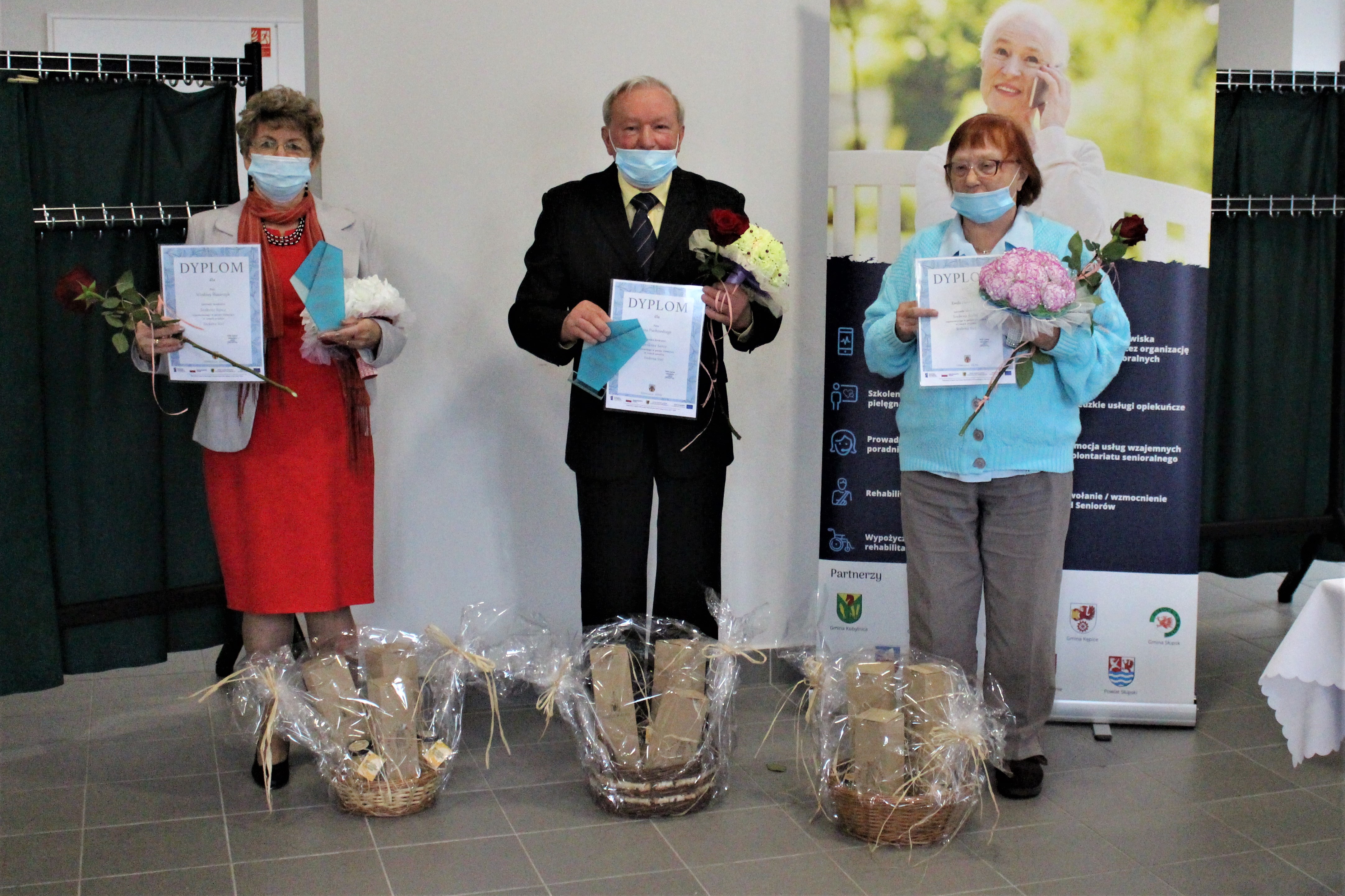Troje laureatów konkursu z dyplomami, bukietami kwiatów oraz nagrodami.