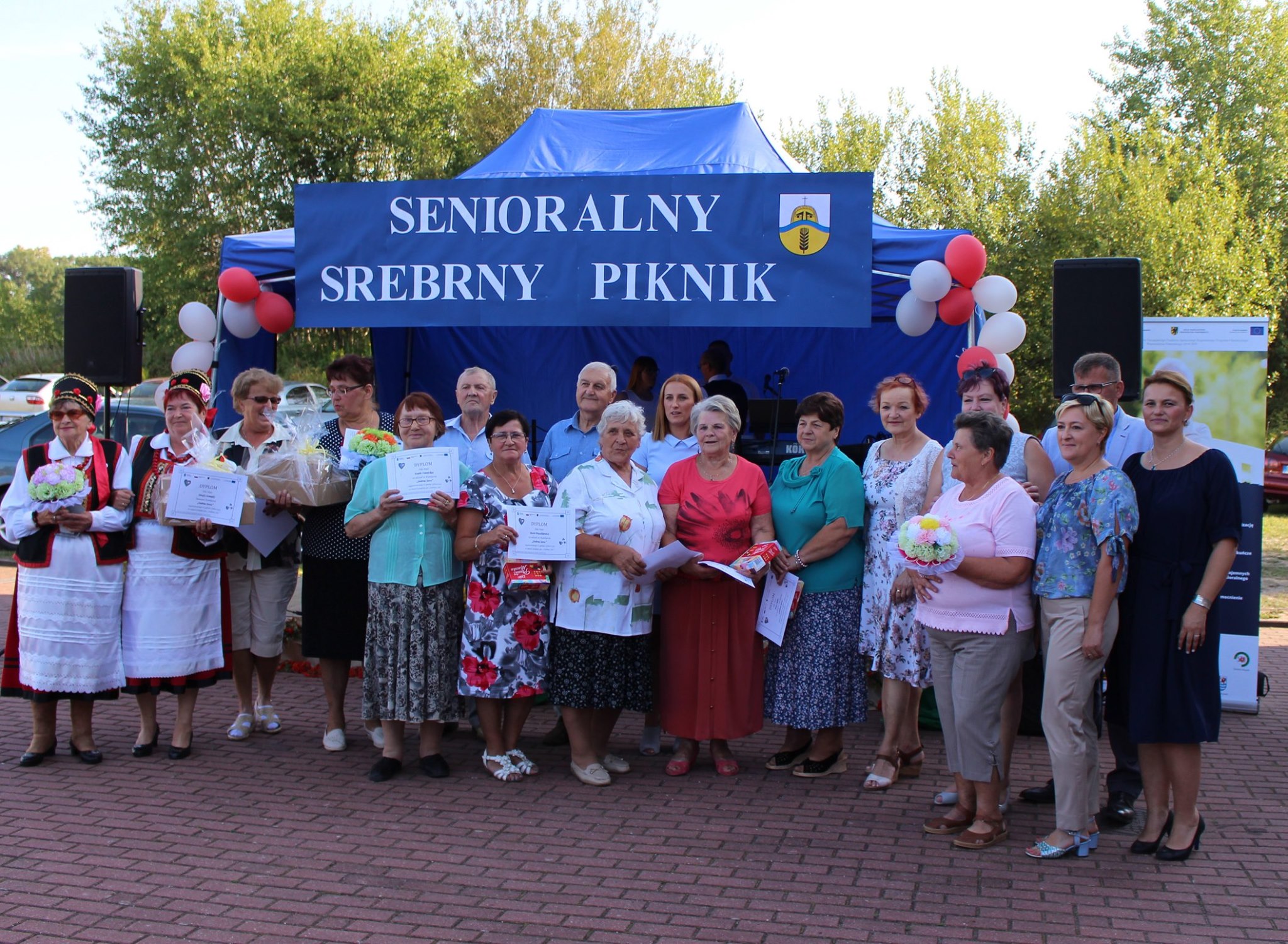 Seniorzy biorący udział w konkursie Srebrne Serce pozujący do zdjęcia z otrzymanymi dyplomami oraz laureaci konkursu z nagrodami.