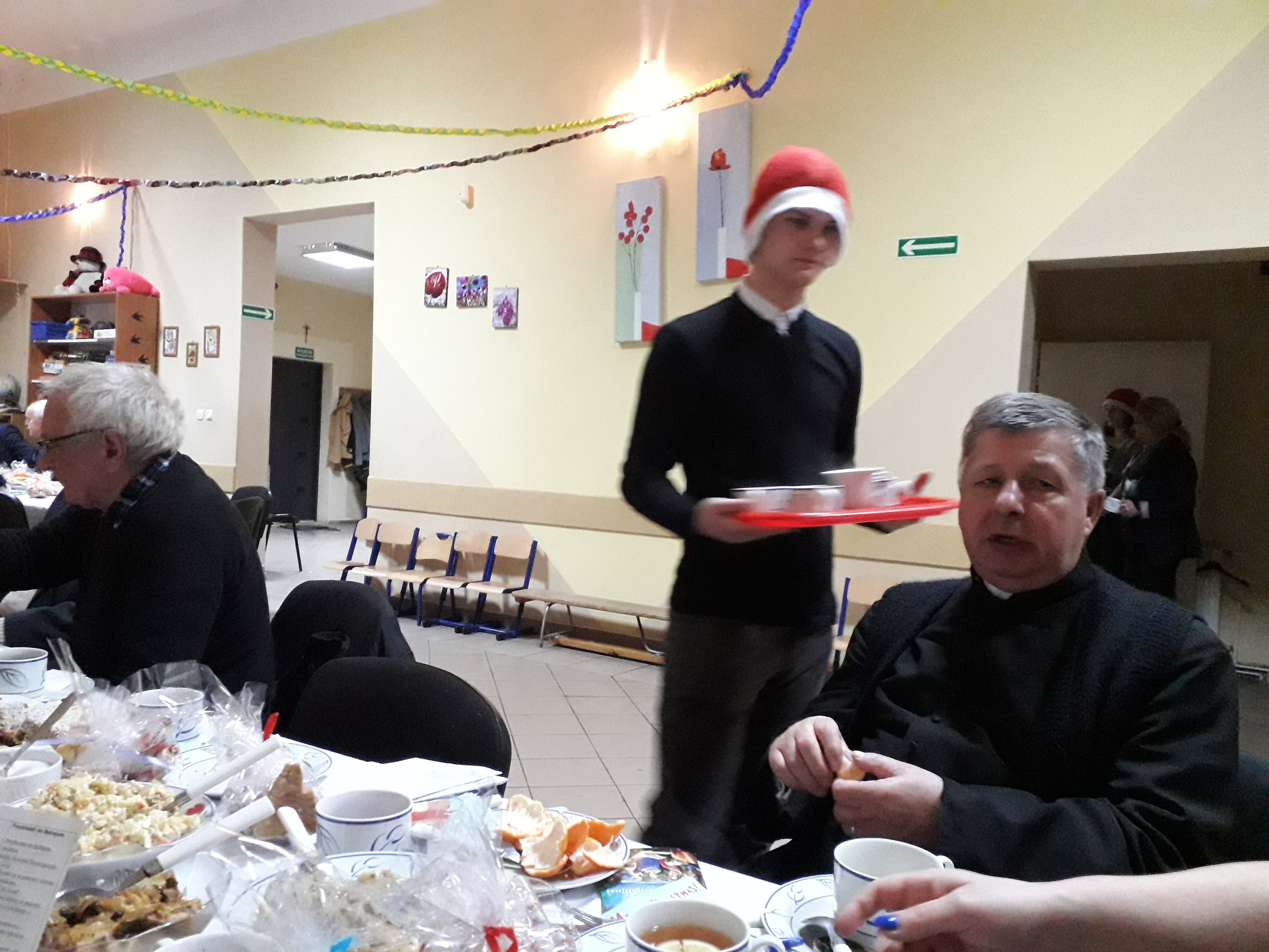 Uczestnicy spotkania przy wigilijnym stole oraz obsługujący ich wolontariusze