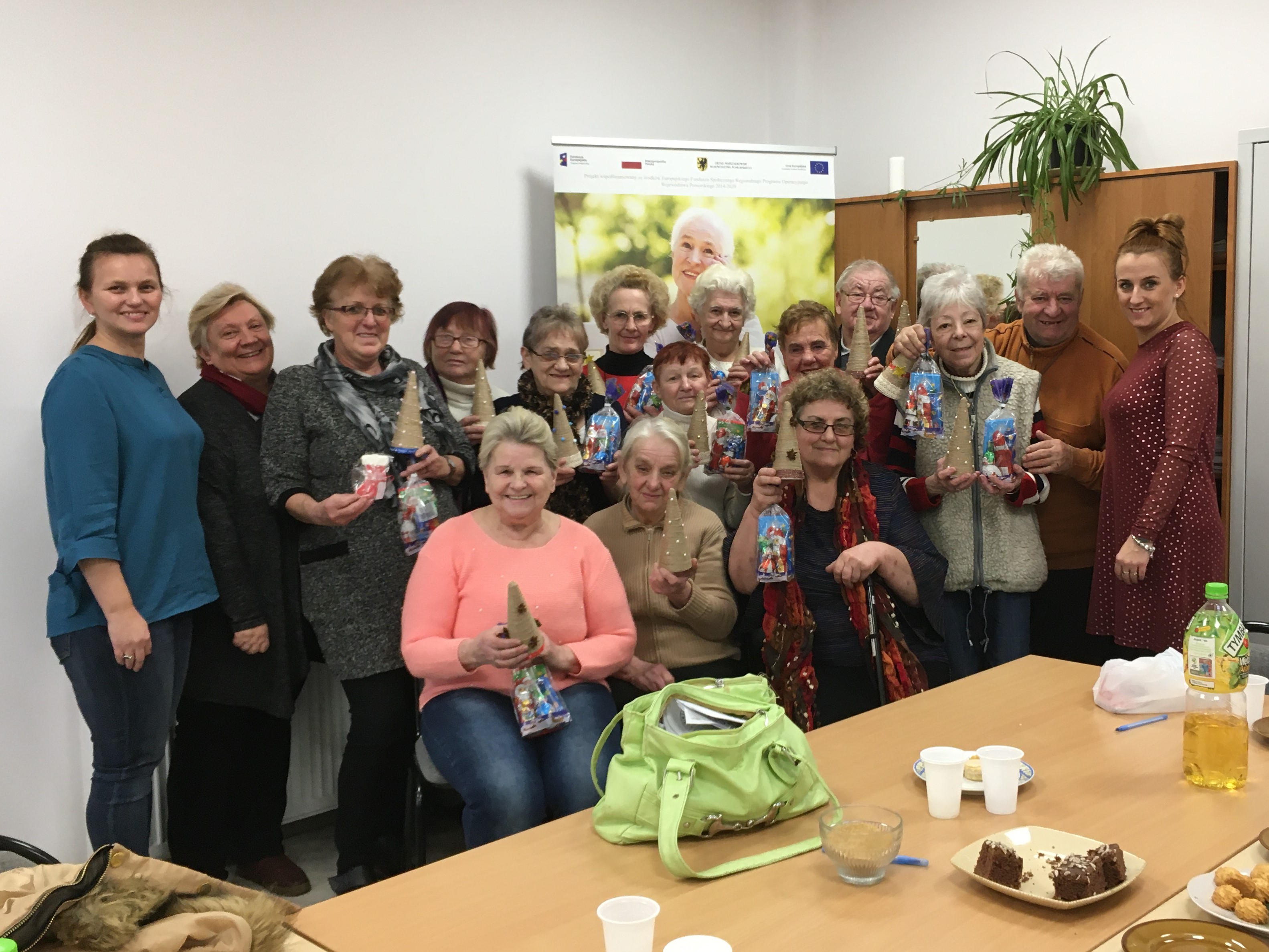 Pozujący do zdjęcia wraz z otrzymanymi słodyczami seniorzy w towarzystwie trenerek prowadzących szkolenie, animatora projektu Srebrna Sieć oraz opiekuna wolontariatu senioralnego.